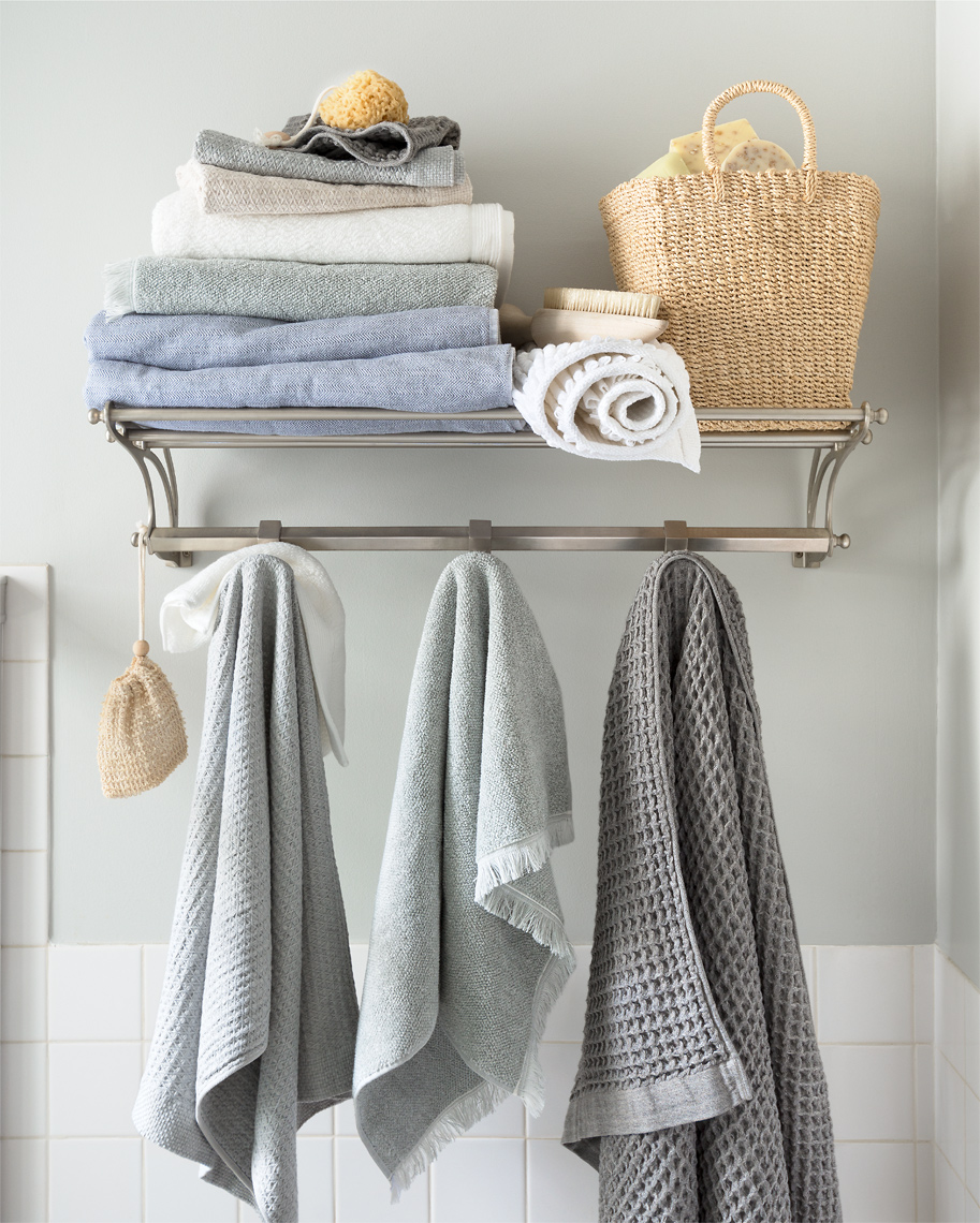 Bathroom towel rack with white, grey, pale blue towels and a whicker basket.